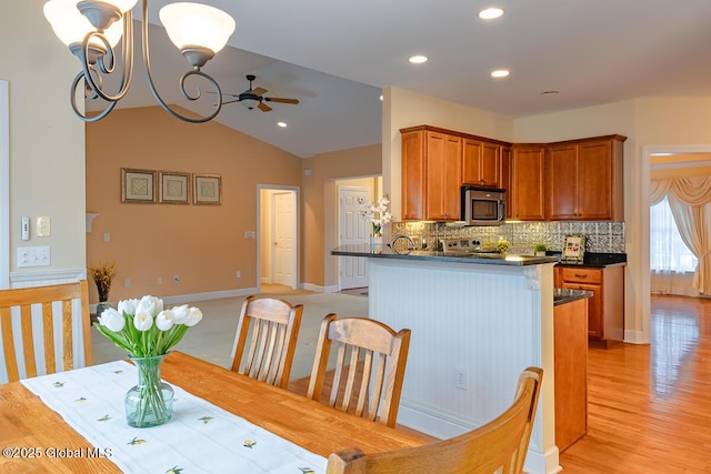 dining area featuring light wood-style flooring, ceiling fan with notable chandelier, recessed lighting, baseboards, and vaulted ceiling