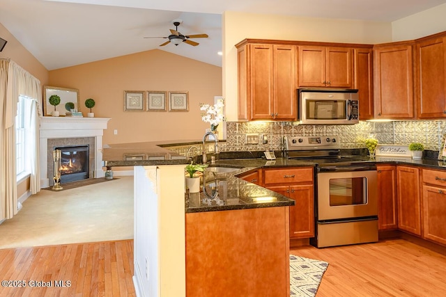 kitchen with a sink, dark stone countertops, appliances with stainless steel finishes, a peninsula, and vaulted ceiling