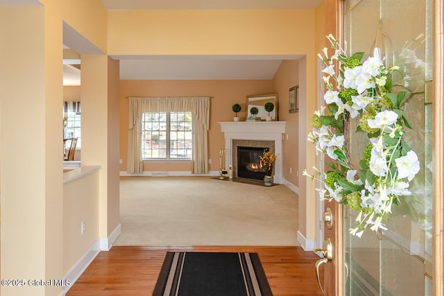 entrance foyer featuring a fireplace with flush hearth, light wood-style flooring, light colored carpet, and baseboards