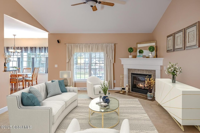 living area with baseboards, a tiled fireplace, light colored carpet, vaulted ceiling, and ceiling fan with notable chandelier