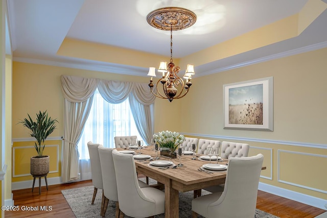 dining area with a tray ceiling, ornamental molding, wainscoting, wood finished floors, and a decorative wall