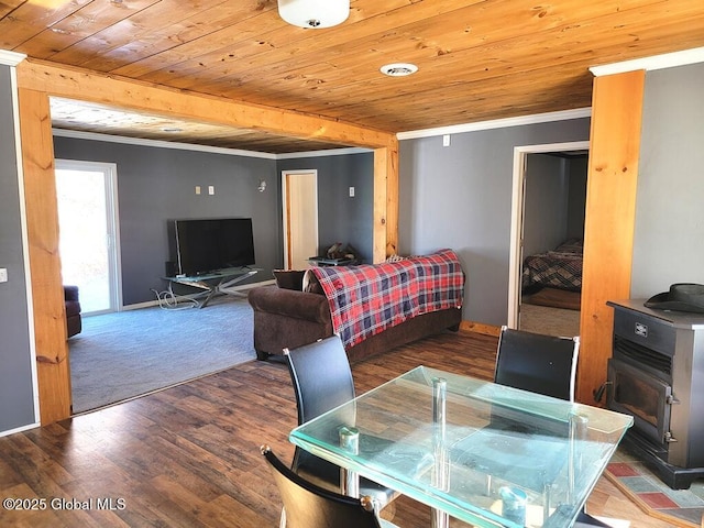 dining room featuring wood finished floors, wood ceiling, baseboards, a wood stove, and crown molding