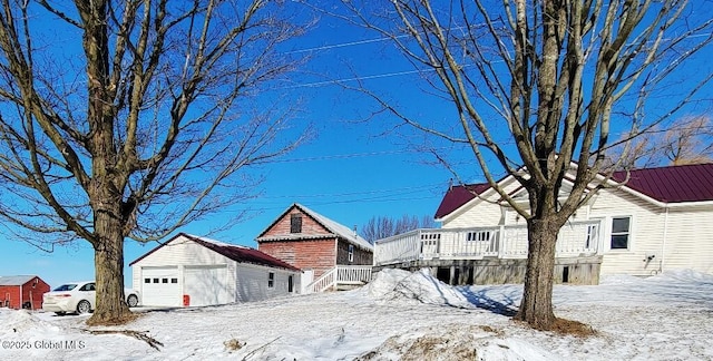 yard covered in snow with a detached garage, a wooden deck, and an outdoor structure