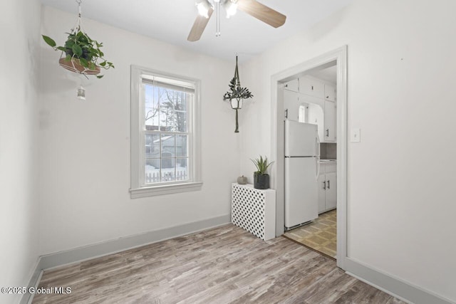 unfurnished dining area with light wood-style flooring, baseboards, and a ceiling fan