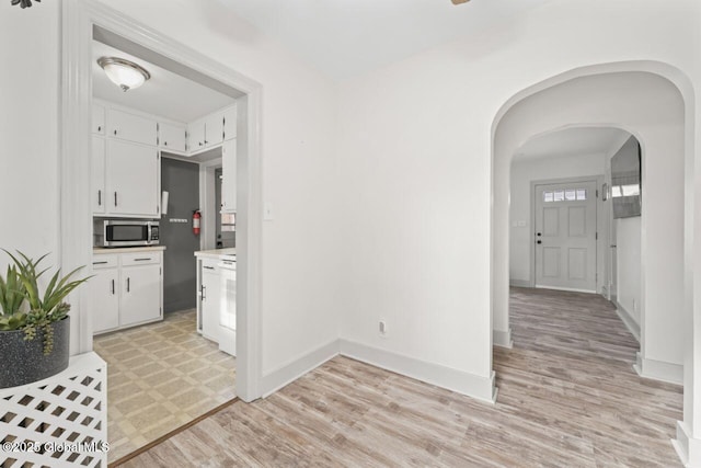 kitchen with arched walkways, white cabinets, stainless steel microwave, light countertops, and light wood-style floors