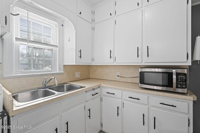 kitchen with a sink, white cabinetry, light countertops, backsplash, and stainless steel microwave