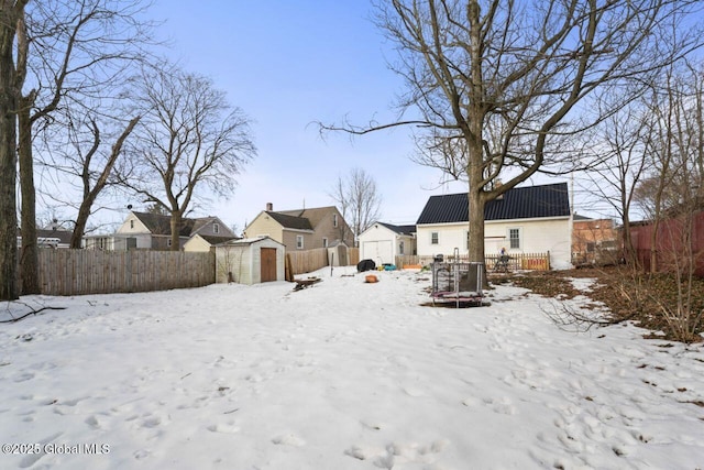 yard covered in snow featuring a garage, an outbuilding, fence, a storage unit, and a deck