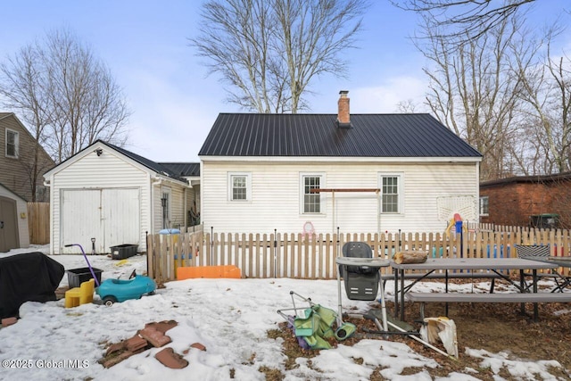 snow covered property featuring an outbuilding, metal roof, a garage, fence, and a storage unit