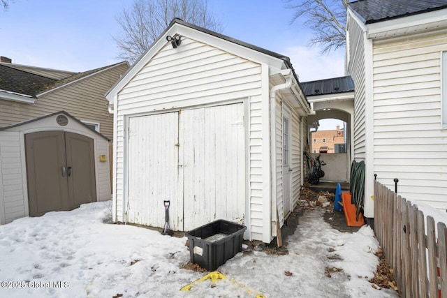 snow covered structure with an outbuilding, a storage unit, and fence