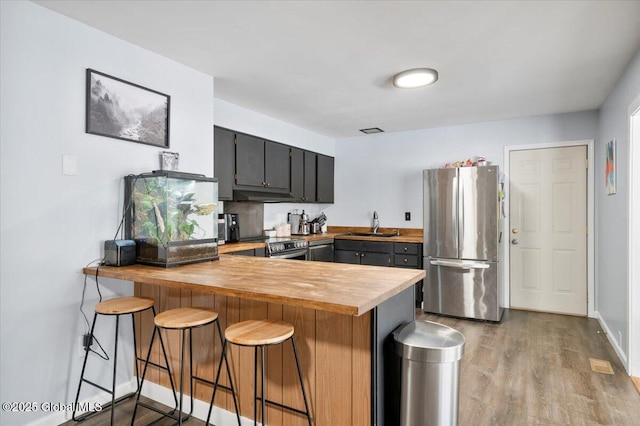 kitchen featuring light wood finished floors, a kitchen breakfast bar, a peninsula, stainless steel appliances, and light countertops