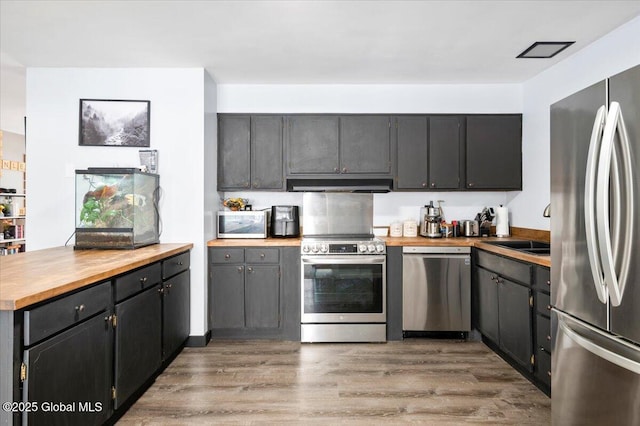 kitchen featuring a sink, light wood-style floors, wooden counters, appliances with stainless steel finishes, and range hood