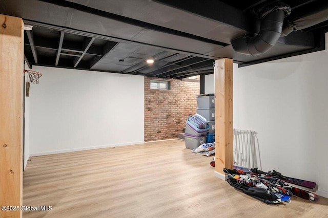 below grade area featuring brick wall, wood finished floors, and baseboards