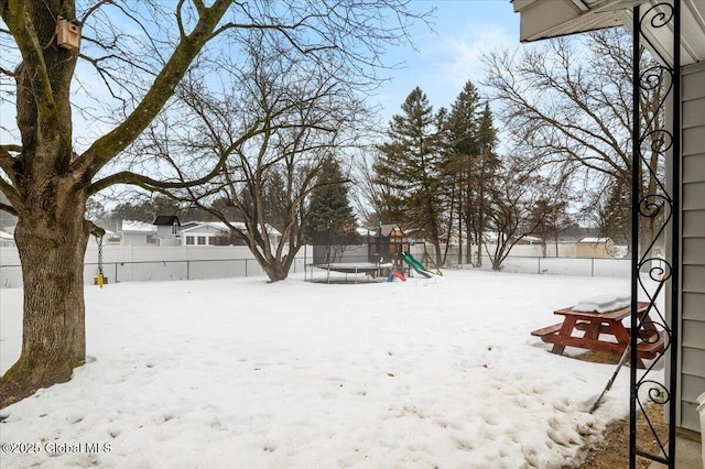 yard layered in snow with a fenced backyard, a trampoline, and a playground