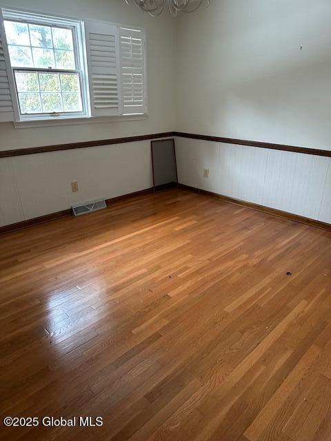 empty room featuring a wainscoted wall, light wood finished floors, and visible vents