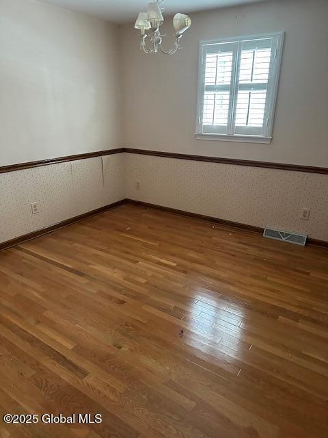 unfurnished room featuring a notable chandelier, visible vents, wainscoting, wood finished floors, and wallpapered walls