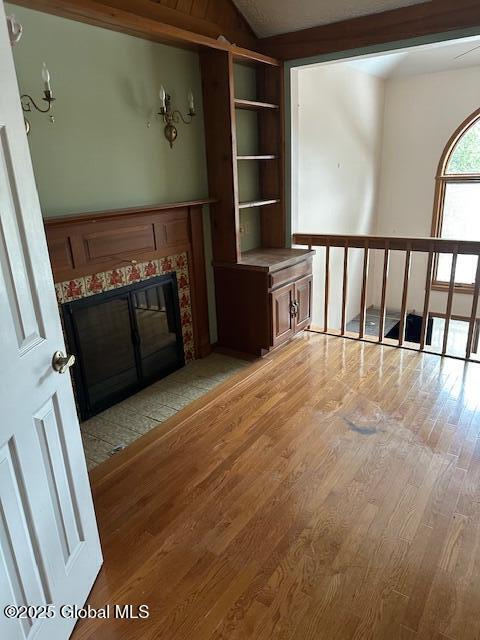 unfurnished living room with vaulted ceiling, light wood finished floors, and a tiled fireplace