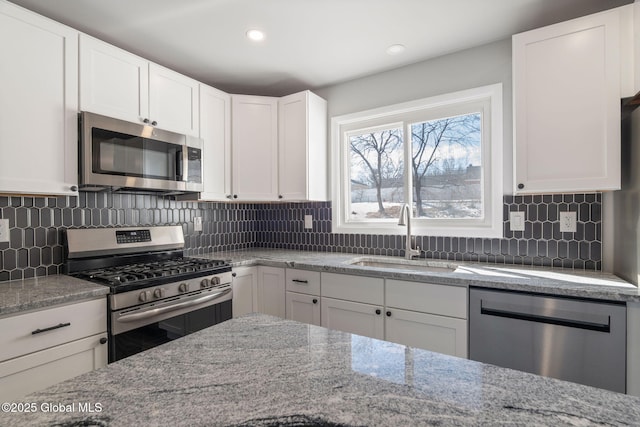 kitchen with tasteful backsplash, white cabinets, light stone countertops, stainless steel appliances, and a sink