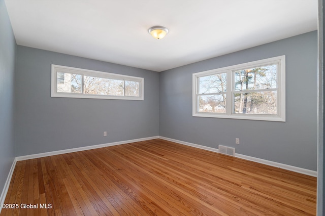 empty room featuring wood-type flooring, visible vents, and baseboards