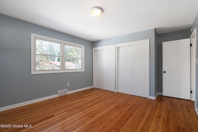 unfurnished bedroom featuring baseboards, wood finished floors, visible vents, and multiple closets