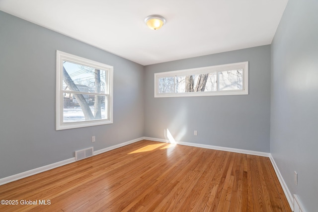 spare room featuring light wood-type flooring, visible vents, and baseboards