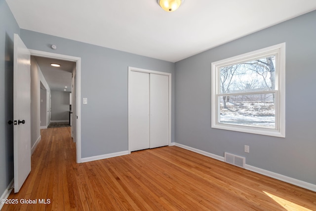 unfurnished bedroom featuring light wood-style floors, baseboards, visible vents, and a closet