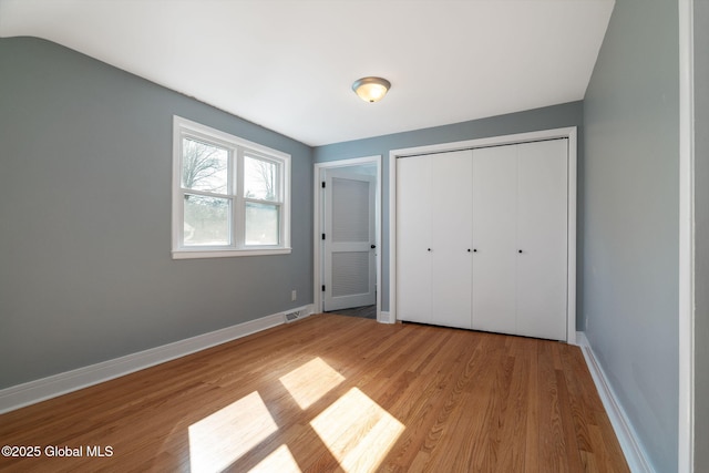 unfurnished bedroom with visible vents, a closet, baseboards, and wood finished floors