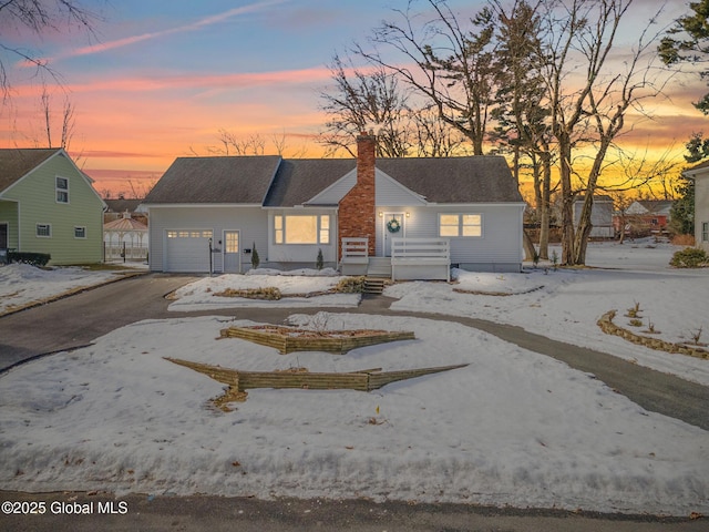 ranch-style home with an attached garage, a chimney, and aphalt driveway