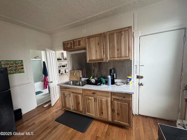 kitchen featuring light wood-style flooring, freestanding refrigerator, an ornate ceiling, a sink, and brown cabinets