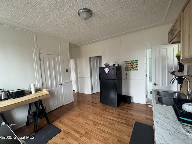 kitchen featuring light wood finished floors, freestanding refrigerator, an ornate ceiling, a sink, and light countertops