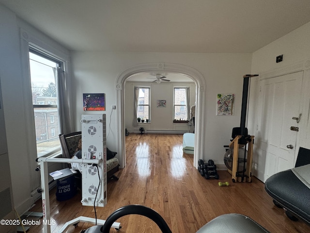 entrance foyer with wood finished floors, baseboards, a baseboard radiator, arched walkways, and ceiling fan