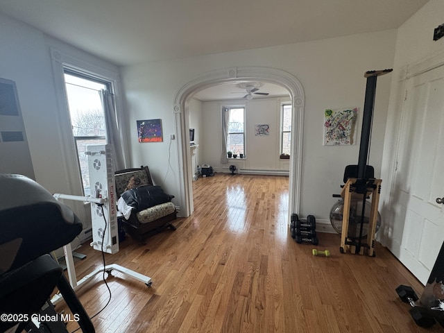 interior space with arched walkways, light wood-type flooring, and a baseboard radiator