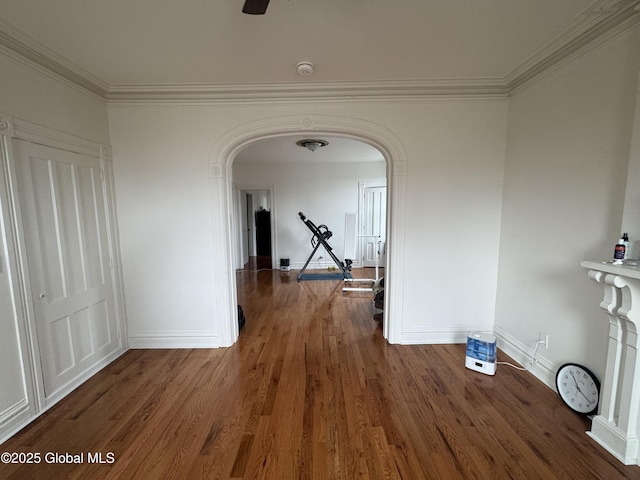 hall featuring baseboards, wood finished floors, arched walkways, and ornamental molding