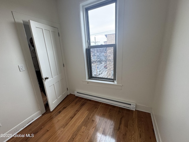 empty room with a baseboard heating unit, baseboards, and wood-type flooring