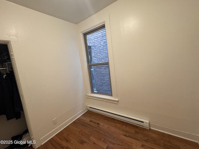 unfurnished bedroom with a baseboard heating unit, wood finished floors, baseboards, and a closet