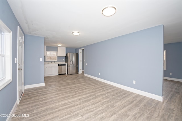 unfurnished living room with baseboards, light wood-type flooring, and a sink