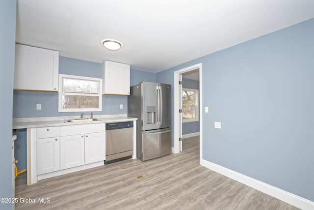 kitchen featuring a sink, light wood-style floors, appliances with stainless steel finishes, white cabinets, and light countertops