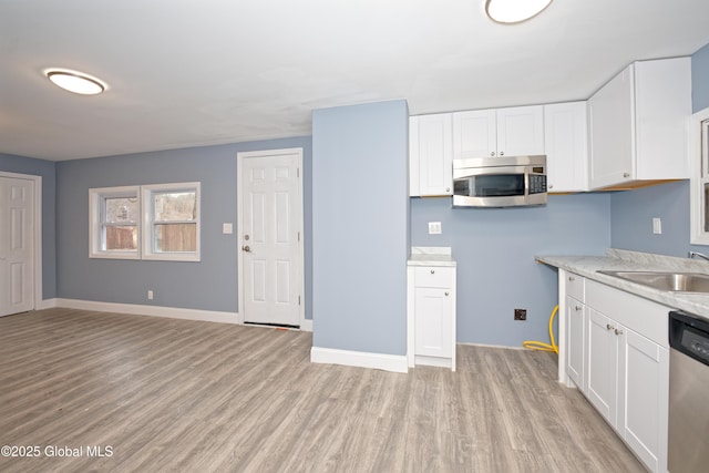 kitchen with light wood finished floors, light countertops, appliances with stainless steel finishes, white cabinetry, and a sink