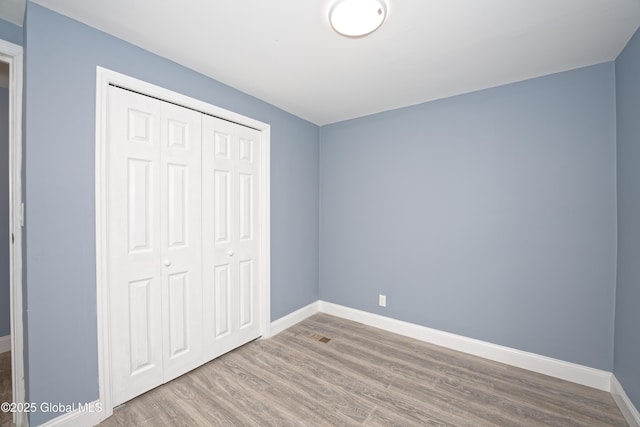 unfurnished bedroom with wood finished floors, baseboards, and a closet