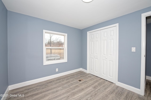 unfurnished bedroom featuring a closet, visible vents, baseboards, and wood finished floors