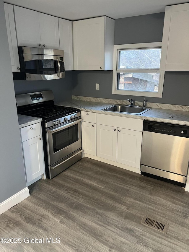 kitchen featuring visible vents, a sink, stainless steel appliances, dark wood-type flooring, and white cabinets