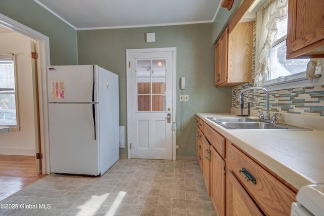 kitchen featuring tasteful backsplash, light countertops, freestanding refrigerator, plenty of natural light, and a sink