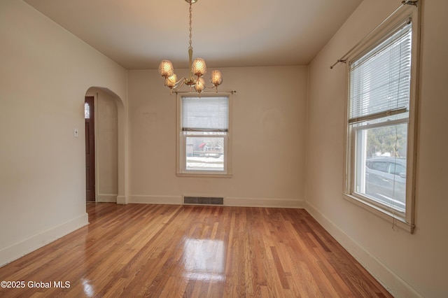 spare room featuring light wood-type flooring, visible vents, arched walkways, and a chandelier