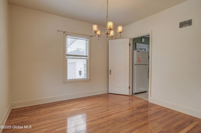 spare room featuring light wood-style floors, visible vents, baseboards, and a notable chandelier