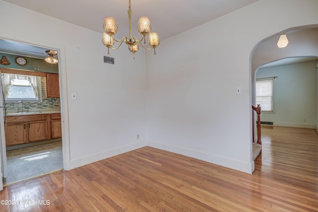 spare room with arched walkways, light wood-style flooring, baseboards, and a sink