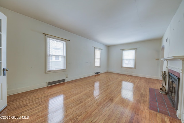 unfurnished living room with visible vents, a fireplace with flush hearth, baseboards, and light wood-style flooring