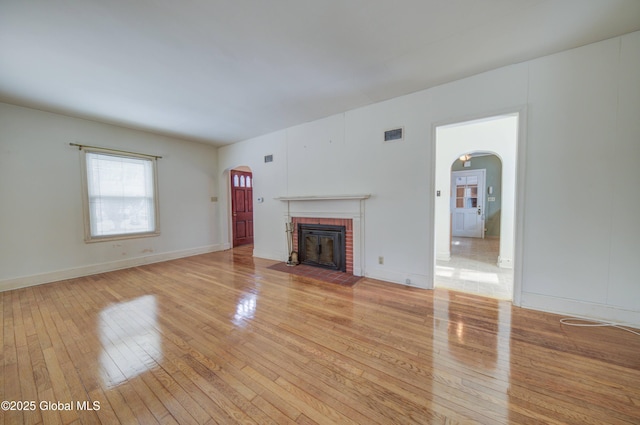 unfurnished living room with light wood-type flooring, arched walkways, visible vents, and a fireplace