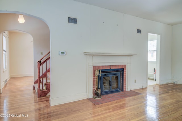 unfurnished living room featuring stairs, a brick fireplace, visible vents, and light wood finished floors