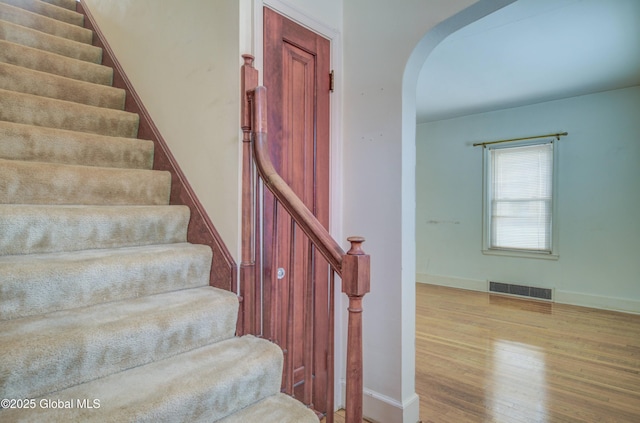 staircase with visible vents, arched walkways, baseboards, and wood finished floors