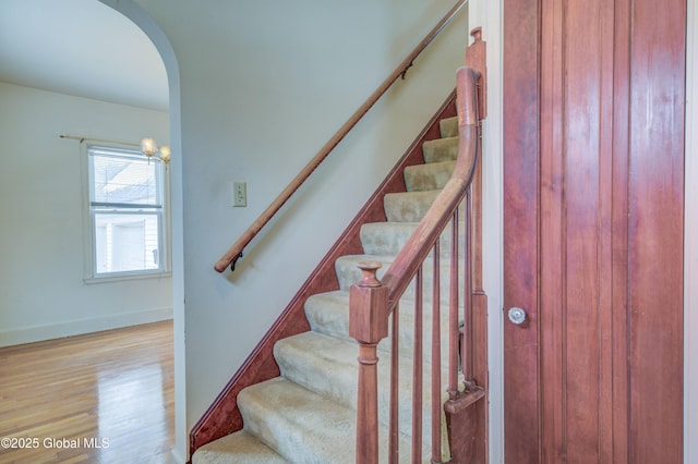 stairway featuring baseboards, arched walkways, and wood finished floors