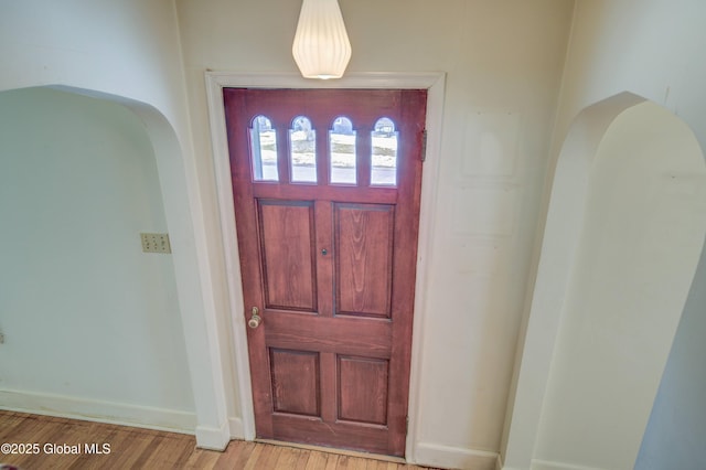 foyer entrance featuring light wood-style flooring, arched walkways, and baseboards